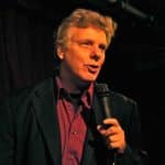 Frank Vignola on stage in a red shirt, holding a microphone