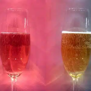 Two Champagne flutes 2/3 full of Champagne, with bubbles and a very colorful red and pink background